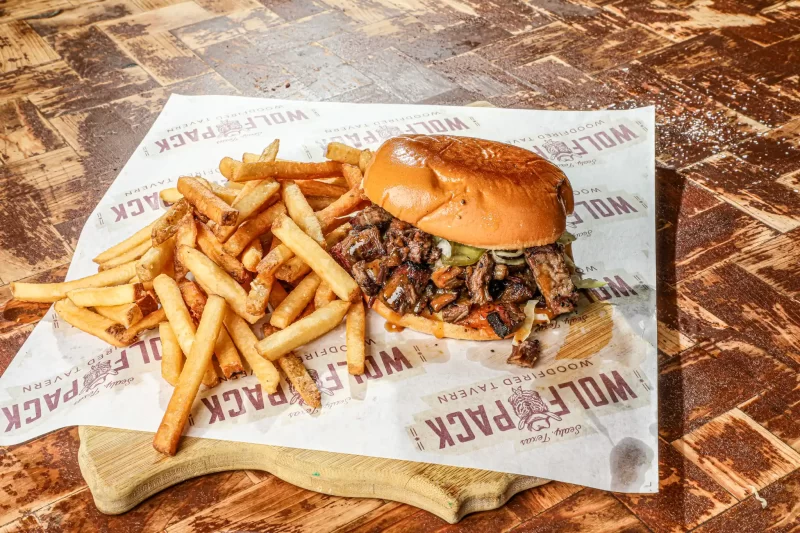 Juicy wood-fired hamburger with melted cheese, lettuce, tomato, and pickles on toasted bun at Wolfpack Woodfired Tavern in Sealy, Texas