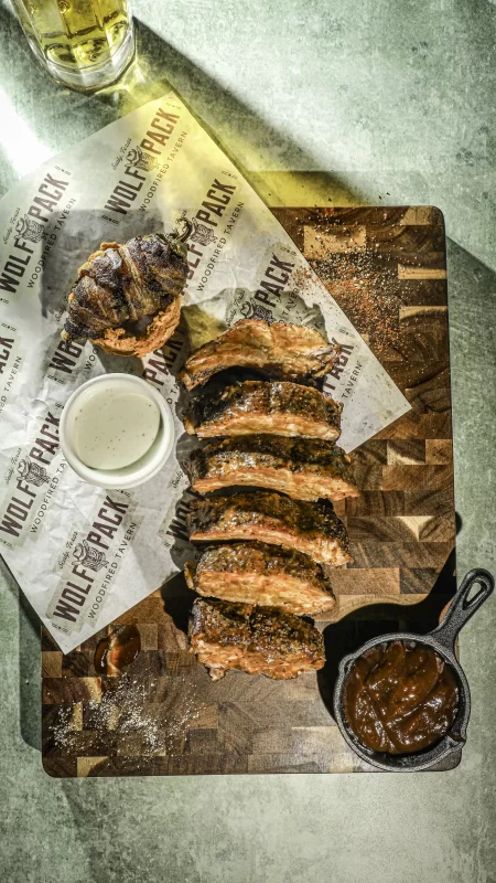 Full rack of wood-fired BBQ pork ribs with classic sides at Wolfpack Woodfired Tavern in Sealy, Texas